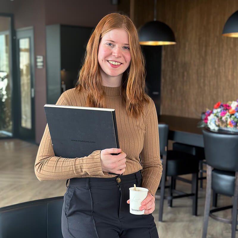 Isabel met boek en koffie leunend tegen stoel